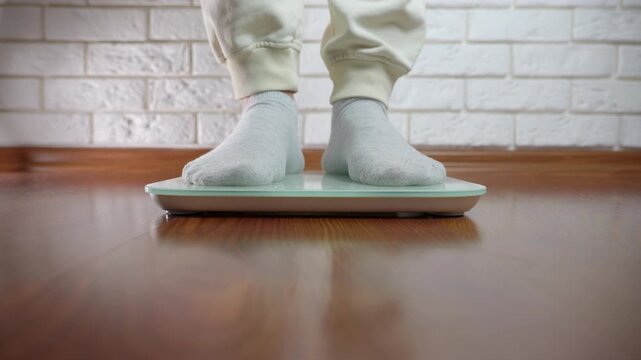 Person stepping on digital scale to measure body weight. Man's feet in socks stepping on a digital floor scale to measure his body weight, representing a healthy lifestyle, diet, and fitness tracking