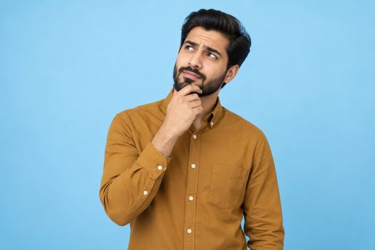 Unsure young man with a beard wearing a brown shirt looking away on a blue background.