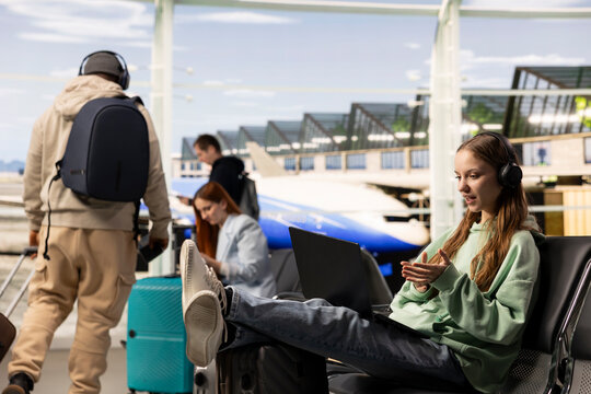 Gen Z woman joins a video conference call on airport internet, speaking with colleagues in an online meeting while seated in the terminal waiting area.