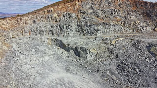 The scene shows a quarry with large rock formations and loose gravel scattered across the ground. Heavy machinery is present for the stone extraction process. Dust is in the air from recent work.