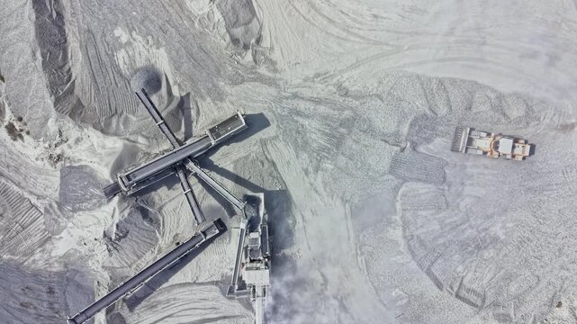 Aerial view of a quarry with large machinery and equipment visible on the surface. The ground shows marked patterns and material that has been excavated.