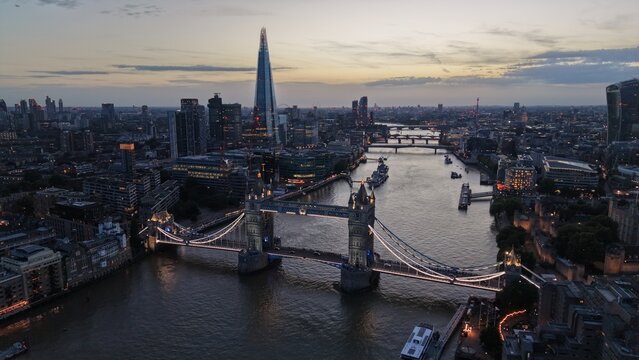 Elevated panoramic view across London at dusk with illuminated Tower Bridge in the foreground, The Shard dominating the skyline and the River Thames stretching into the distance.