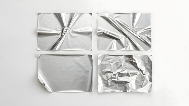 Four rectangular sheets of crumpled silver aluminum foil with different textures and folds arranged on a plain white background surface