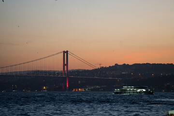 Obraz premium Illuminated ferry passing under the Bosphorus Bridge at dusk, Istanbul