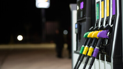 Purple, yellow and green fuel nozzles on a gas station pump at night © janvaneyck