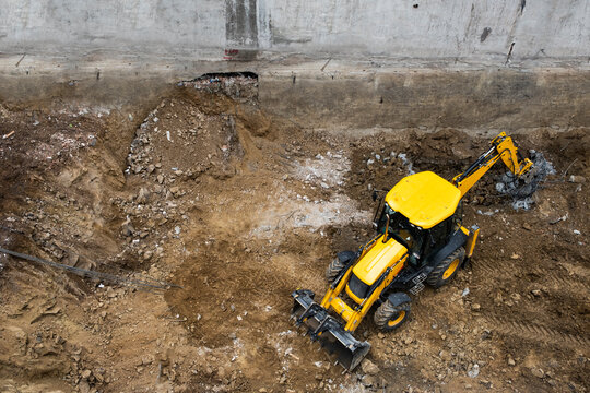 Yellow backhoe loader digging in a muddy construction pit, high angle