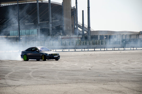 BMW E46 coupe drifting with tire smoke on an empty lot by a stadium