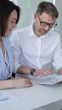 Business professionals collaborating around a desk, analyzing reports and tablet data, planning strategy and making decisions in a modern office meeting