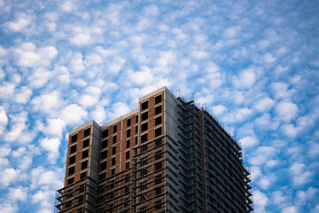 Unfinished high-rise building with scaffolding under a cloudy blue sky © Burak