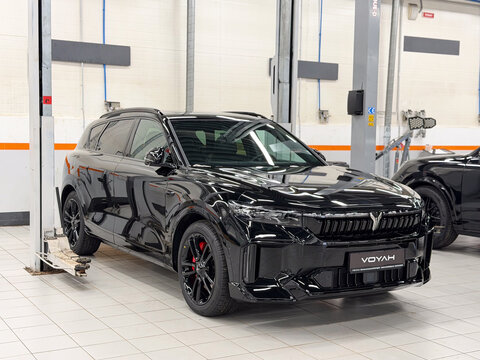Black Voyah Free Sport Edition 4WD EREV hybrid SUV car with a 1.5L turbo engine and 490 hp electric motors parked on a lift platform inside a dealership showroom repair shop. Premium Chinese vehicle.