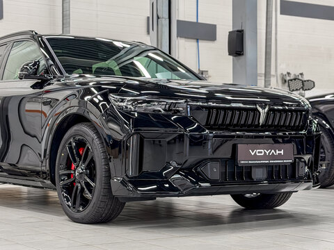 Black Voyah Free Sport Edition 4WD EREV hybrid SUV car with a 1.5L turbo engine and 490 hp electric motors parked on a lift platform inside a dealership showroom repair shop. Premium Chinese vehicle.
