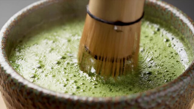 Traditional matcha tea preparation with a bamboo whisk creating froth