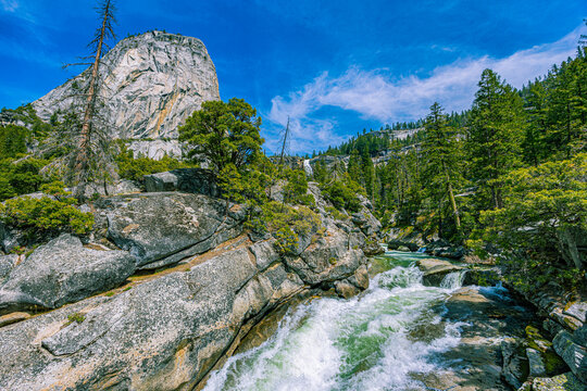 Whitewater rapids of the Merced River flowing over granite bedrock with the iconic Liberty Cap dome rising in the background.