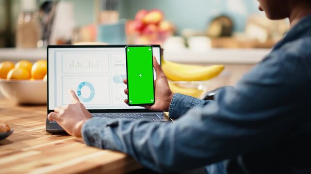 Vertical green screen on mobile phone near laptop with analytics data, modern lifestyle scene with chroma key for infographic elements and digital tools.