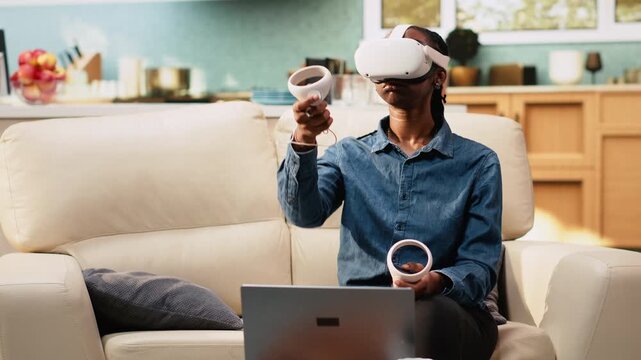 Woman freelancer works with virtual reality headset for futuristic simulation and 3D motion tracking during innovative multitasking. Young adult uses VR metaverse technology at home.