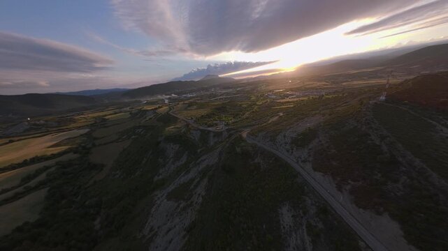 Wide first person FPV flight revealing an open rural valley with patchwork fields winding roads and several small villages beneath layered mountain ridges in the Pyrenees