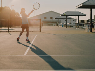 Young tennis player hitting a backhand shot on an outdoor tennis court at sunrise. © visualstory