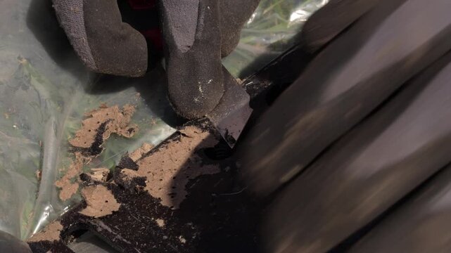 Video of gloved hands using a utility knife to scrape dirt off a surface, detailed cleaning and restoration process close-up