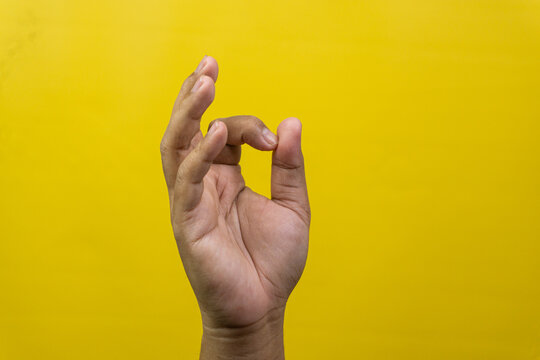 One male hand is raised showing precise pinching motions representing relaxed approval against bright yellow background, Thumb gently touches index digit forming small circles while