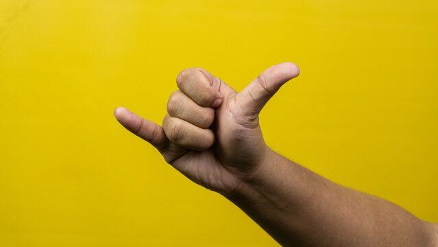 A single male hand displays the classic shaka sign or telephone gesture positioned centrally over a vibrant yellow background, The thumb and pinky finger are fully extended outward