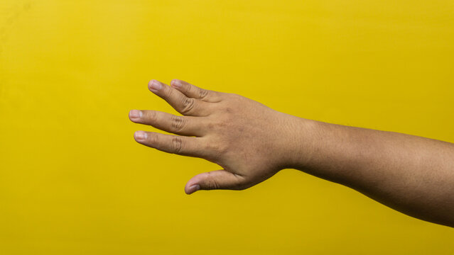 A male hand is extended horizontally with fingers spread apart reaching downward against a vivid yellow background, The posture suggests an attempt to grab an item touch a surface