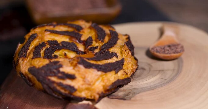 Brown choux pastry ring with chocolate chips, baked round pastry ring lies on a dark surface next to a chocolate piece, light