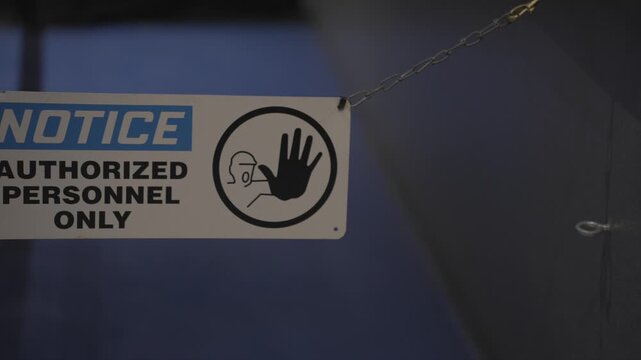 A restrictive safety sign reading "Notice: Authorized Personnel Only" hanging from heavy metal chains, blocking off restricted access to a secured area. The barrier creates a strong visual boundary.