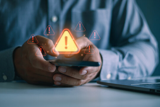 Businessman using smartphone with cybersecurity warning icon, illustrating mobile phishing, online scam, cyber attack, digital fraud, data protection, network security, privacy risk awareness.