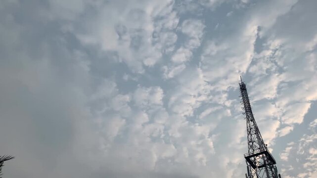 Telecommunication tower silhouette against dramatic altocumulus clouds cloudy sky. Low angle view
