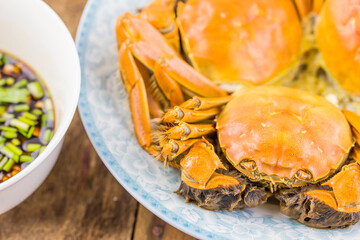Steamed orange-red crabs served on a plate with a small bowl of dipping sauce on wooden table. © tai