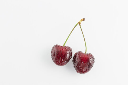 Two ripe, red cherries with water droplets are displayed on a plain white background, showcasing their fresh, glossy texture.