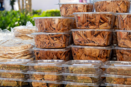 Multiple clear plastic food containers filled with homemade, crusty baked pita bread chips. The bite-sized square snacks are golden brown. The whole-grain pita food is for sale at a farmers' market. 