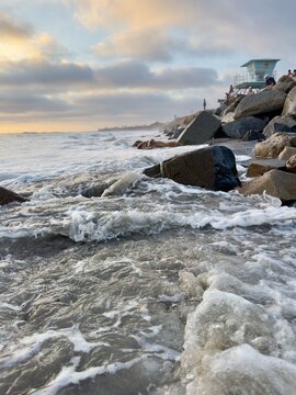 Low-angle portrait view of surging high tide ocean water flowing past rock riprap at Ponto Beach in Carlsbad, California.
