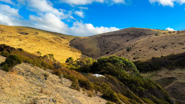 Vast rolling hills and grassy mountain valleys under a bright blue sky with fluffy white clouds