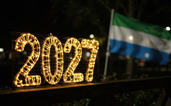 Glowing 2027 New Year lights decoration next to a national flag at night