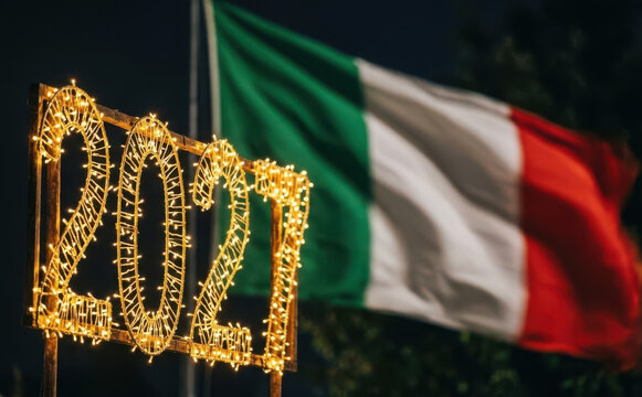 Italian flag waving proudly at night next to illuminated 2027 glowing holiday lights decoration for New Year celebration