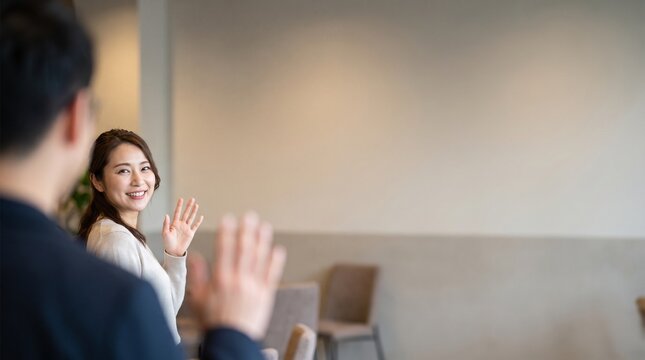 カフェやオフィスで笑顔で手を振り親しい同僚や知人に挨拶をする若い女性   