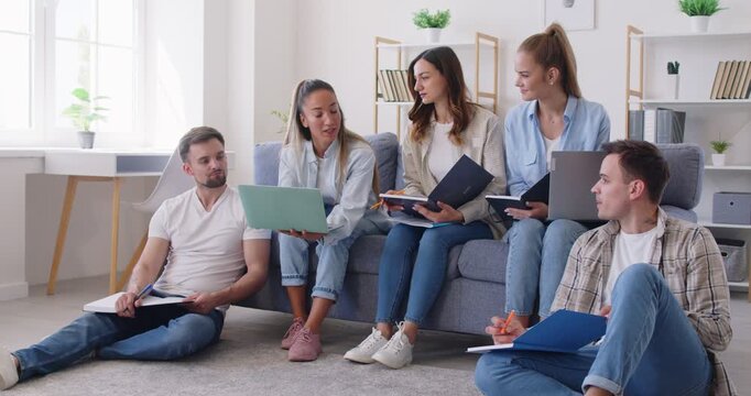 Group of a young cheerful people students sitting on sofa in living room at home and studying indoors preparing for test together discussing learning. Education and knowledge concept. 4k video.