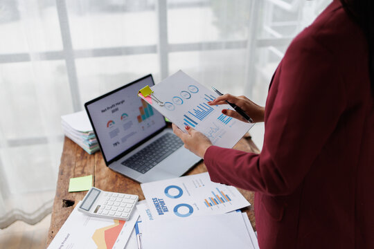 Businesswoman analyzing financial data reports and charts on documents and laptop screen, performing data analysis for corporate growth and economic planning