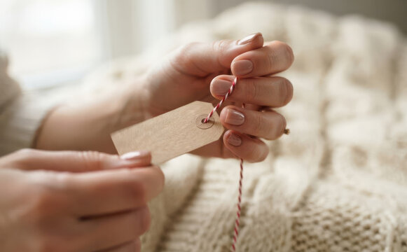 Woman holding blank brown paper price tag with red and white string for handmade product branding