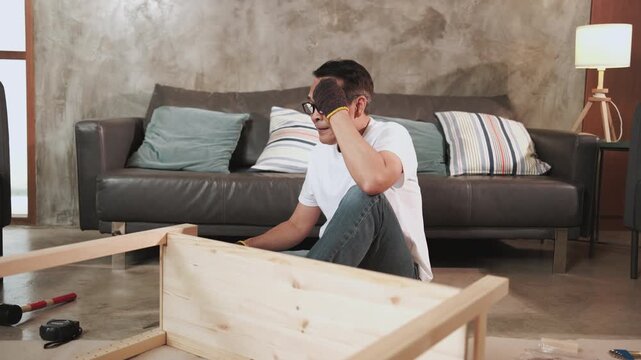 Asian mature man self-assembling carpentry furniture with DIY tools, tightening with screwdriver, tired and resting at living room sofa, home improvement, craft installation, hobby wooden workshop.