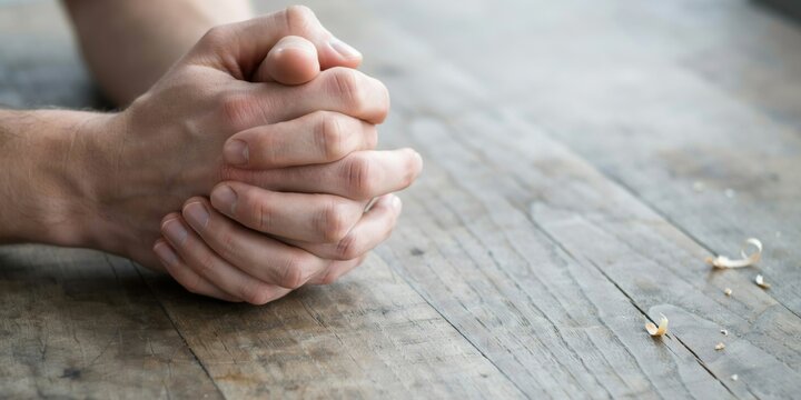 Hands folded together in prayer on a wooden surface, showing concentration and hope