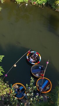 Vertical screen Aerial Departing Coracles In Hoi An With Vietnamese Passengers Leaving Dock At Dusk, Soft Reflections On River, Colorful Round Boats And Tranquil Farewell Mood