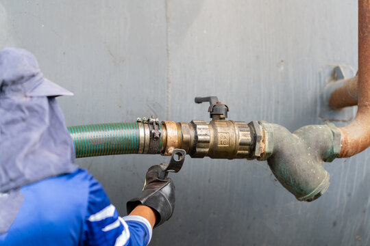 Close-up of a technician attaching a green flexible discharge hose to an industrial pipe and valve mechanism.