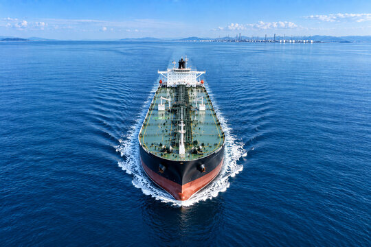one large modern crude oil tanker centered on a vast calm blue sea, clean symmetrical composition, subtle distant refinery infrastructure barely visible along the horizon
