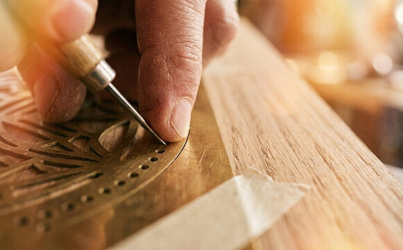 Close up of an artisan hands carving intricate patterns on wood and metal with precision tools for handmade crafts