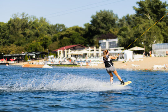 Female wakeboarder wakesurfing. Girl riding waterski cabel. Holding tow rope. Summer activities in the lake.