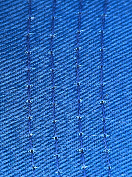 Macro view showing navy blue fabric texture stitched with parallel vertical seams captured using sharp industrial photography style