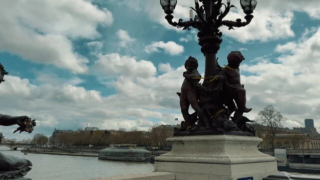 Sculptures on Pont Alexandre III overlook the Seine River and distant Eiffel Tower with cruise boats sailing under cloudy Parisian skies during a scenic daytime visit to France.

