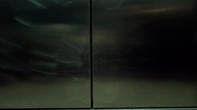Sliding elevator doors close and reopen inside a building, revealing a marble staircase with a metal handrail in an empty hallway.